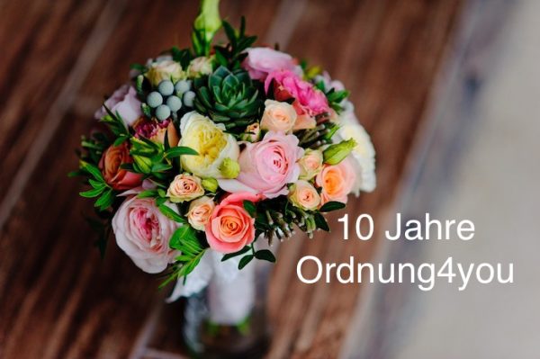 Ein bunter Blumenstrauß steht auf dem Tisch, darunter steht: 10 Jahre Ordnung4you.