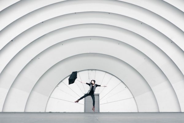 Frau tanzt mit einem Regenschirm befreit auf einer Kuppelbühne. Erleichterung pur, Wegschmeißen ohne schlechtes Gewissen. 