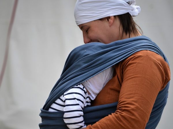 Eine Mutter trägt ihr Baby glücklich lächelnd im Tragetuch. Mama-Glück!