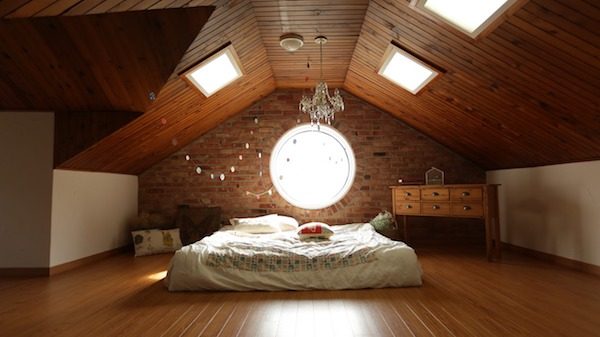 Unter einer Dachschrägen steht ein Bett, der Fußboden aus Holz ist aufgeräumt und frei.