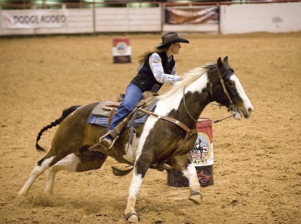Eine Rodeoreiterin lenkt ihr Pferd schnell und impulsiv um eine Tonne. Schnelle Ordnung.