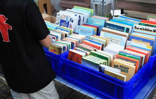 Ein Junge steht vor einer blauen Box mit Büchern. Ordnung und Flohmarkt.