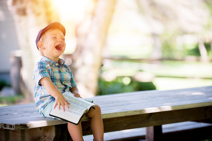 Ein kleiner Junge sitzt auf einer Bank und lacht herzhaft. Ordnung mit Spaß!