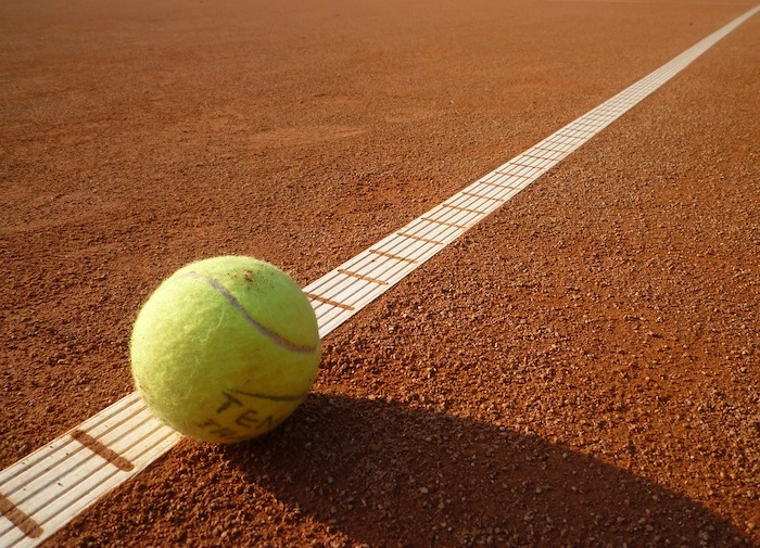 Ein gelber Tennisball liegt an einer weißen Grenze des Tennisplatzes.