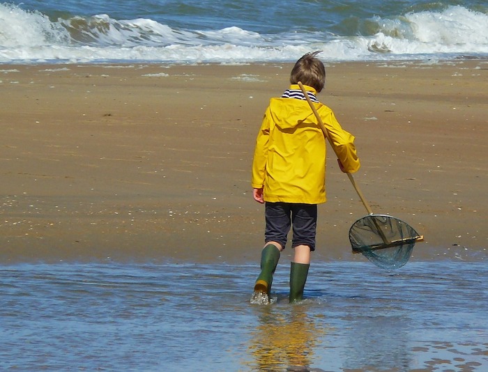 Ein Kind läuft mit einem Fischernetz am Strand. Sachen-Fang!