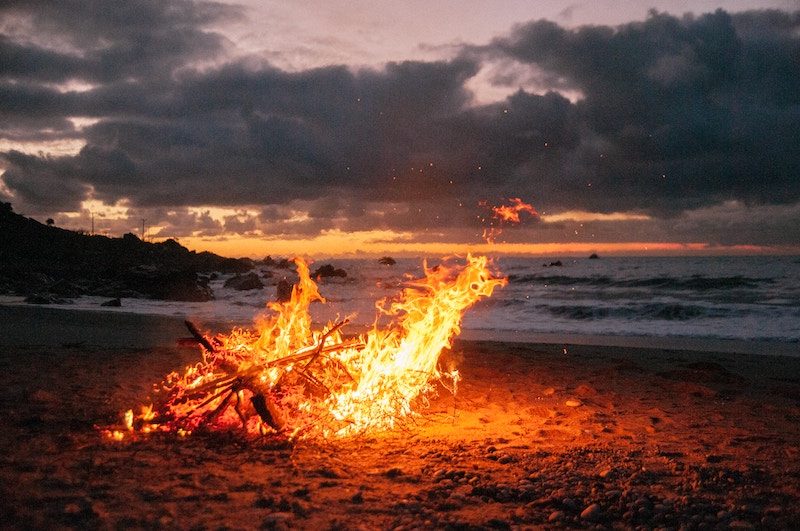 Ein Feuer brennt herunter im Sand am Meer. Ausgebrannt. Ordnung gegen Burnout.
