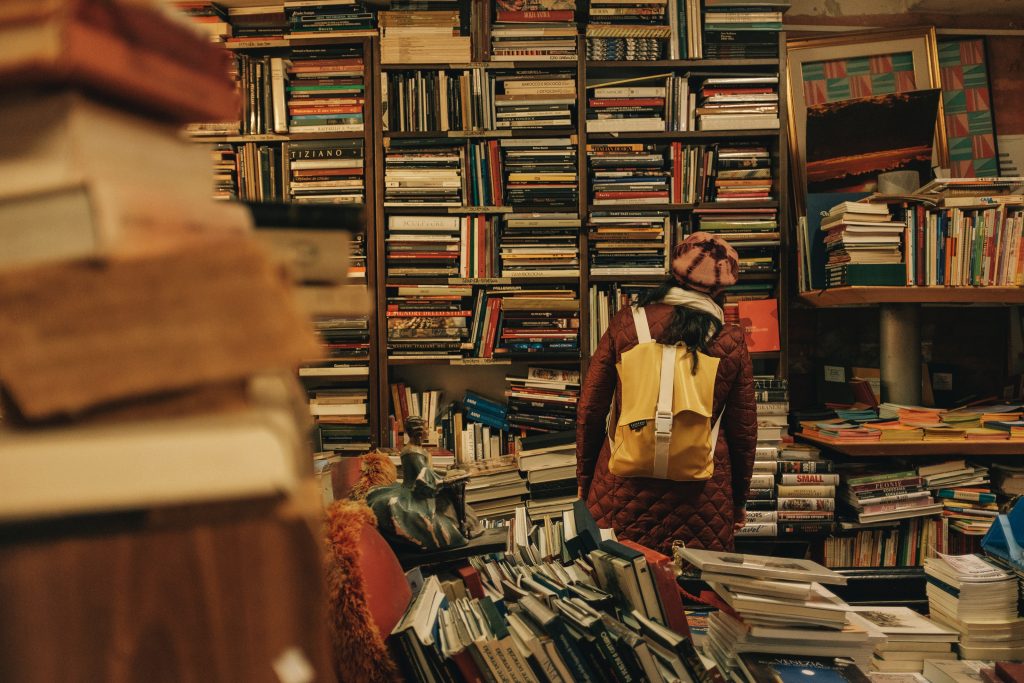 Eine Frau mit Rucksack steht in einem Raum mit hunderten von Büchern. Chaotisch. Messie-Syndrom? 