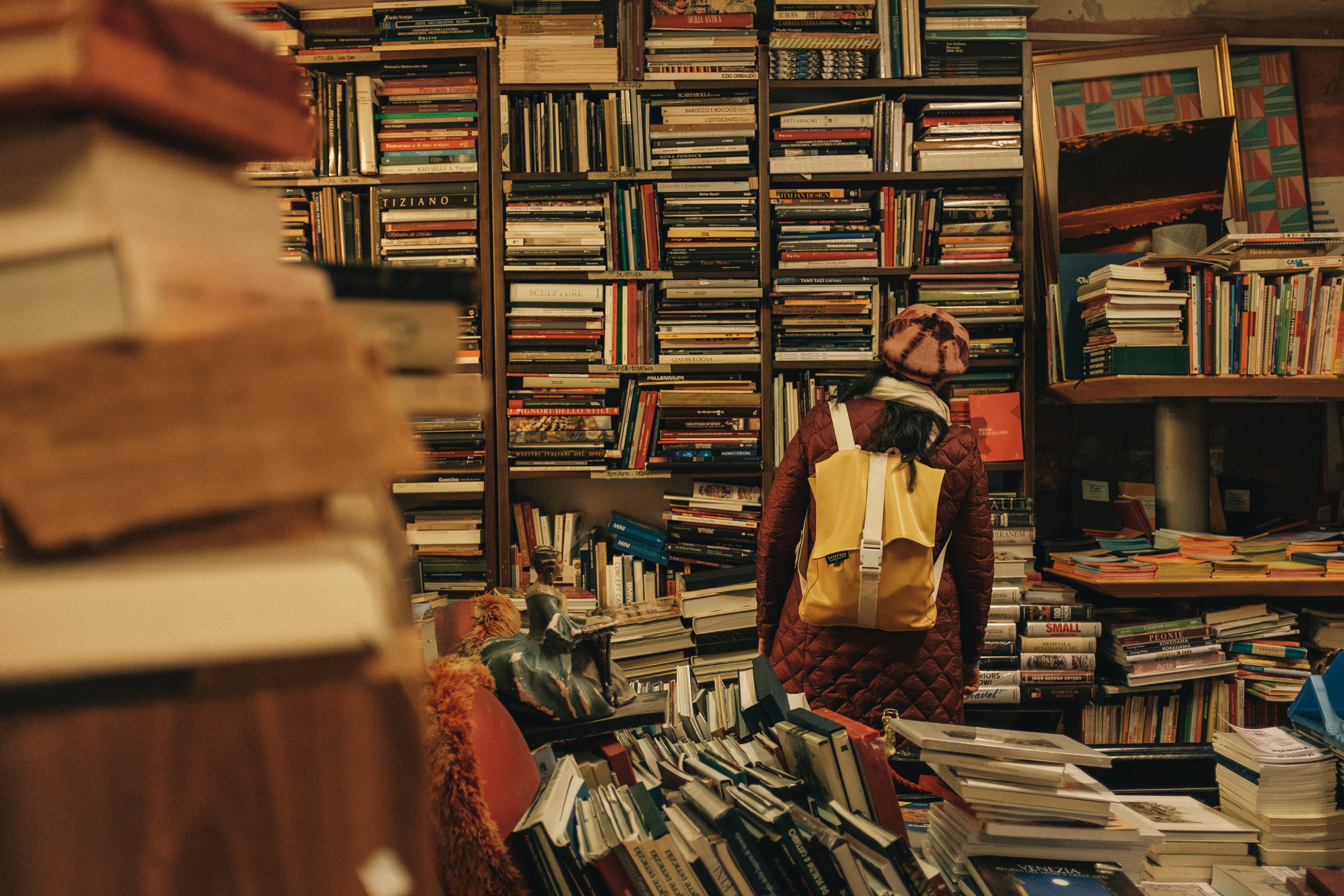 Eine Frau mit Rucksack steht in einem Raum mit hunderten von Büchern. Chaotisch. Messie-Syndrom?