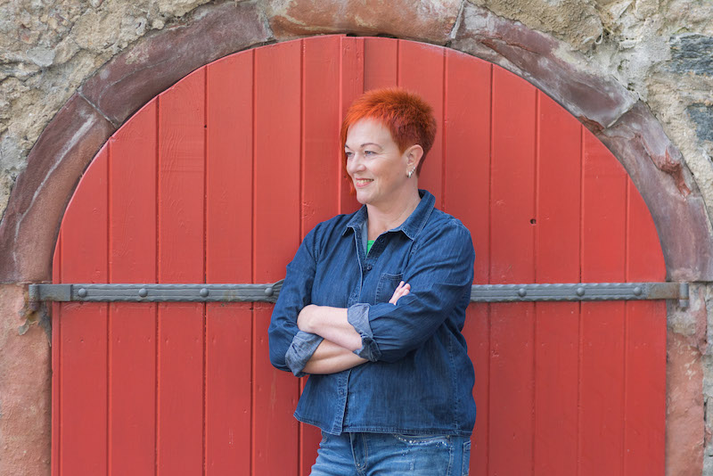 Heike Eberle von Ordnung4you steht lächelnd vor einem roten Holztor. Sie bietet echte Ordnungshilfe an. 