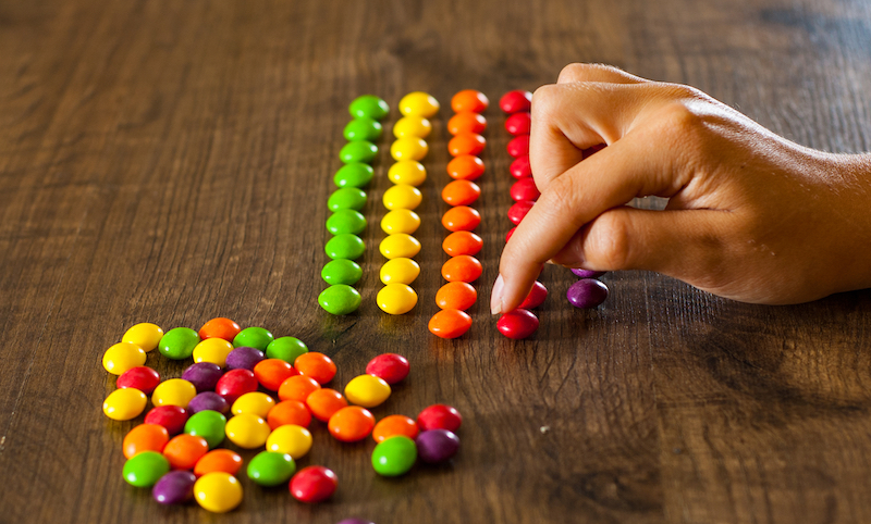 Eine Frauenhand sortiert bunte Drops in farbige Reihen. Zu viel Ordnung?